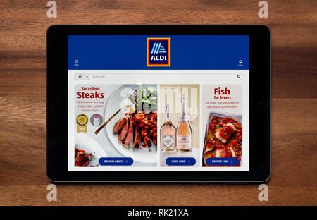 Il sito web di Aldi è visto su un tablet iPad, il quale è appoggiato su un tavolo di legno (solo uso editoriale). Foto Stock