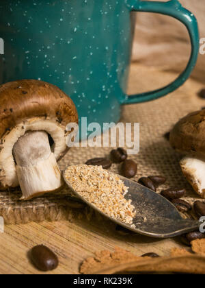 Latte macchiato di funghi in una tazza con i funghi e i chicchi di caffè su una tavola di legno Foto Stock