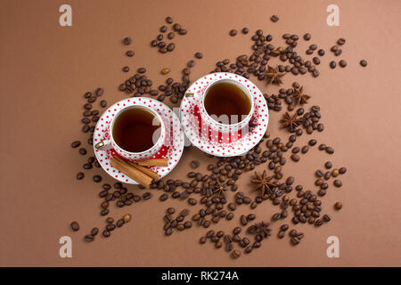 Due piccante di caffè nero polka dot tazze e i chicchi di caffè pasticcio su sfondo marrone Foto Stock