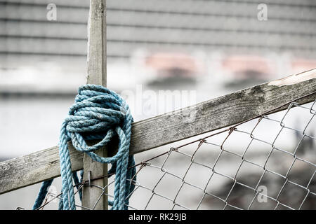 Blue corda avvolta intorno al legno e una rete di recinzione, nave da crociera in background Foto Stock