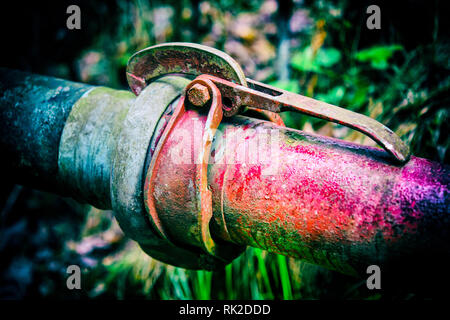 E colorata antica tubi metallici con frizione su sfondo scuro con erba sfocata. Accoppiamento di rosso e blu la pipeline di close-up. La coesione, la connessione fissa. Foto Stock