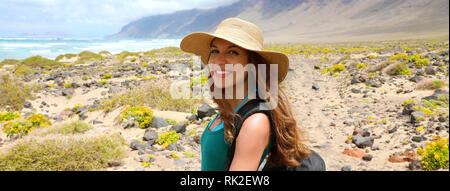 Felice viaggiatore bellissima ragazza con cappello di paglia alla ricerca per la fotocamera. Giovani femmine backpacker esplorare Lanzarote isole Canarie. Panorama di banner. Foto Stock