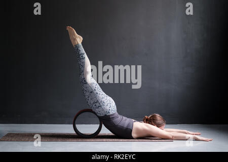 La donna a praticare yoga facendo Shalabhasana utilizzando ruote, Locust pone a piena lunghezza Foto Stock