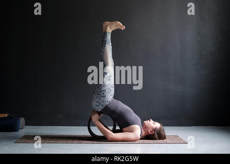 Giovane donna a praticare yoga, in piedi Viparita Karani esercizio, utilizzando ruote Foto Stock