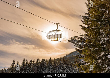 Due sciatori su una seggiovia contro lo sfondo del sole, cielo nuvoloso e coperta di neve alberi, foto di contorno, arancio, regione sciistica di Schladming Foto Stock