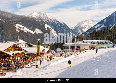 Ristorante Alpino pieno di sciatori, snowboarder e tobogganers sulla giornata di sole. Sullo sfondo la gondola Hochwurzen stazione di sci, montagne innevate. Foto Stock