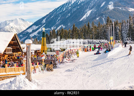 Ristorante Alpino pieno di sciatori, snowboarder e tobogganers sulla giornata di sole. Sullo sfondo la gondola Hochwurzen stazione di sci, montagne innevate. Foto Stock