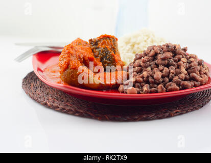 Popolari piatti nigeriani - Fagioli e riso bianco servito con un assortimento di carni in una targhetta rossa Foto Stock