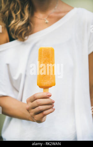 Vegano sano di mango orange citrus gelato ghiaccioli in mano della giovane donna. Estate dessert e allegro estate umore concept Foto Stock