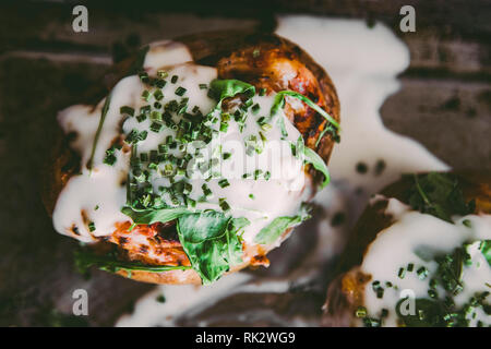 Close up di cosse al forno ripieni di patate con formaggio e panna acida e rucola dal di sopra. Spazio di copia Foto Stock