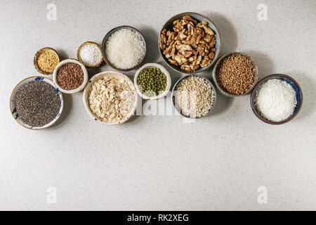 Varietà di materie non cotti i grani di cereale super chia, biancheria, sesamo, Mung bean, noci, tapioca, frumento, grano saraceno, fiocchi d'avena, noce di cocco, riso in ceramica Foto Stock