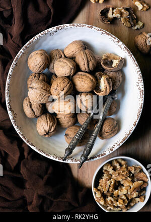 Noci intere e pezzi di noce in ciotole con un dado vintage cracker. Foto Stock