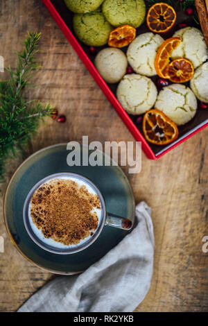 Una tazza di salep turco guarnita con cannella in polvere fotografata su uno sfondo di legno. Accompagnata da pino foglie, melograno arils, una scatola f Foto Stock