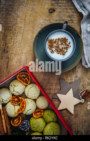 Una tazza di salep turco guarnita con cannella in polvere fotografata su uno sfondo di legno. Accompagnata da una scatola piena di cookies, bastoncini di cannella e o Foto Stock