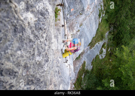 Turista femminile, in colorate sport vestiti, si arrampica su un difficile sezione verticale su una via ferrata al di sopra di Hallstatt, Austria, durante un estate climbi Foto Stock