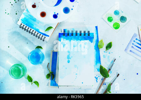 Molla di disegno concetto con gli strumenti dell'artista, il verde e il blu album da disegno ad acquerello, i pennelli e la tavolozza dei colori su uno sfondo luminoso con spazio di copia Foto Stock