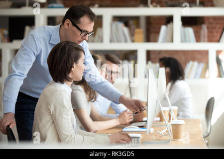 Mentor ceo di supervisore di aiutare il dipendente spiegando computer lavoro in ufficio Foto Stock