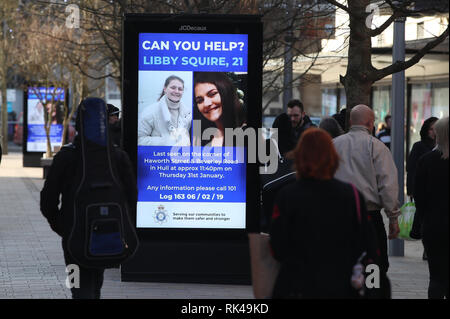 Passanti con visualizzazione digitale di un poster di polizia nel centro di Hull come la ricerca continua per 21-anno-vecchio studente Libby scudiero, che è scomparso dalla sua casa in città dal febbraio 1st. Foto Stock