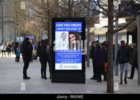Passanti con visualizzazione digitale di un poster di polizia nel centro di Hull come la ricerca continua per 21-anno-vecchio studente Libby scudiero, che è scomparso dalla sua casa in città dal febbraio 1st. Foto Stock