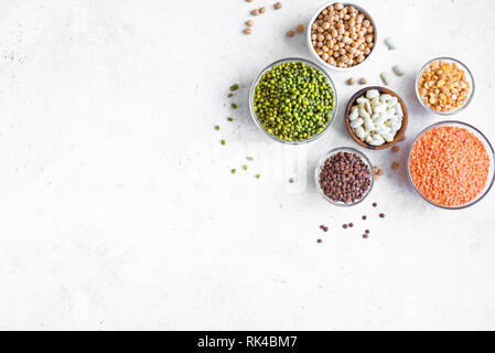 Assortimento di legumi colorati in ciotole, lenticchie, fagioli, ceci, mung, piselli su sfondo bianco, vista dall'alto, copia dello spazio. Cibo sano, dietin Foto Stock