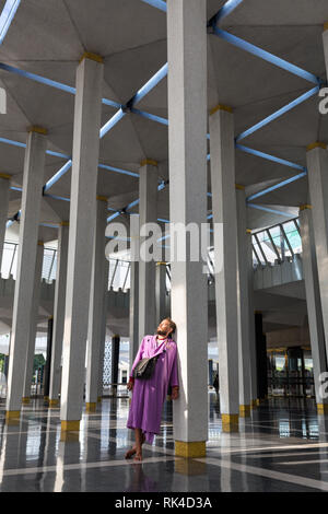 Un maschio di turisti in moschea nazionale della città di Kuala Lumpur sorge vicino alla colonna e gode la bellezza degli interni. Foto Stock