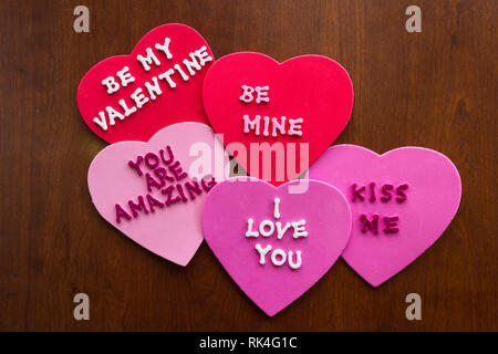 Romantico messaggi scritti con glitter lettere sulla colorata cuori bloccati su un sfondo di legno Foto Stock