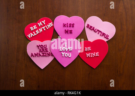 Romantico messaggi scritti con glitter lettere sulla colorata cuori bloccati su un sfondo di legno Foto Stock