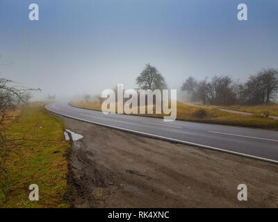 Un solitario strada che conduce nella nebbia orizzonte Foto Stock