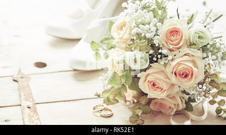 Giorno di nozze composizione con scarpe, le rose rosa fiori bouquet nuziale e gli anelli di nozze visto da un angolo alto su sfondo di legno Foto Stock