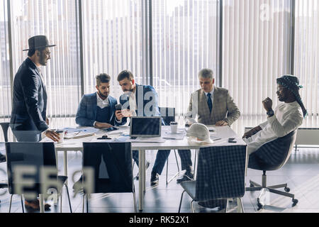 Elegante e ben vestito uomini di affari di diversa età e appartenenza etnica in giacca riuniti per la negoziazione, collaborando in spaziose ufficio moderno m Foto Stock