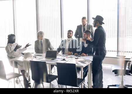 Business meeting tra multirazziale di gestione superiore per i membri del consiglio di amministrazione nel nuovo ufficio moderno sala conferenze con finestre panoramiche e laptop. Foto Stock