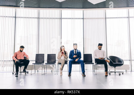 Per i candidati per un nuovo lavoro.La disoccupazione concetto. quattro persone intelligenti sono l'utilizzo dei gadget mentre è seduto in ambienti interni Foto Stock