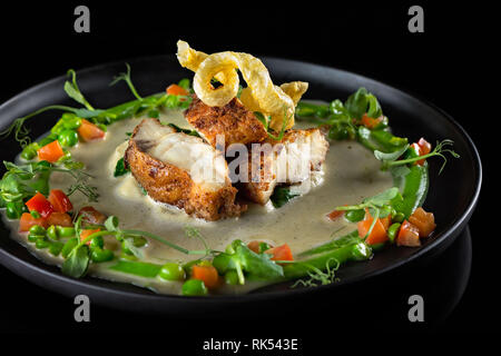 Halibut servito in emulsione con verdura verde su una piastra nera Foto Stock