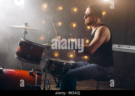 Splendido uomo in jeans e maglietta a fare musica con set di tamburi. vista laterale foto Foto Stock