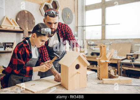 Carpenter la costruzione di una casetta per uccelli in legno insieme con il suo ragazzo. Un piccolo figlio partecipa attivamente in fatto a mano processo. Felice della paternità e del fai da te con Foto Stock