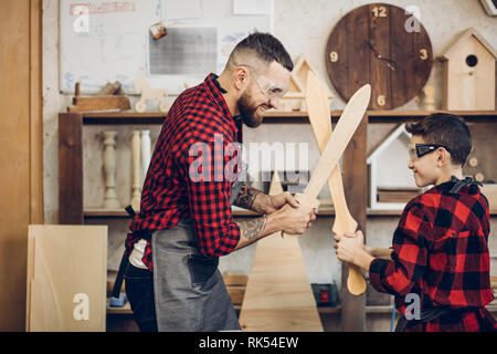 Relazioni familiari, la paternità, hobby, falegnameria, concetto di falegnameria - padre e figlio la riproduzione di cavalieri con legno spade DIY al workshop di falegname Foto Stock