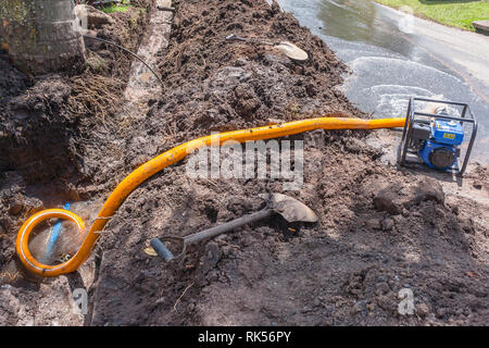 Plumbing lavori di movimento terra Scavo di trincee riparazioni delle rotte principali tubo acqua in strada residenziale area con motore mobile di pompaggio drenaggio sottovuoto danni. Foto Stock