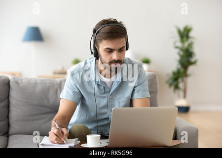 Grave un uomo guarda il computer portatile che indossa la cuffia di apprendimento della lingua straniera Foto Stock