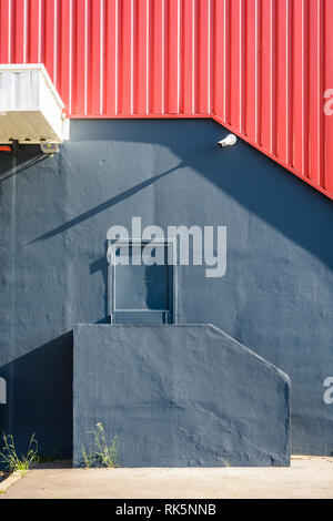 Una porta pedonale nella parete di un grande magazzino, alla sommità di una piccola scalinata, al di sotto di un rosso di ferro ondulato schierandosi con una videocamera di sicurezza. Foto Stock