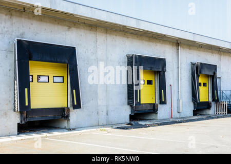 Tre camion di banchine di carico con guarnizioni di tenuta in gomma nel muro di cemento di un magazzino con una chiusa gialla tapparella porta. Foto Stock