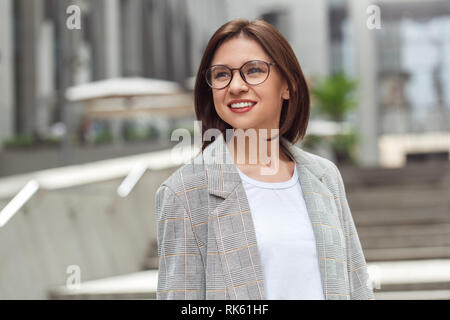 Business casual. Signora giovane in occhiali in piedi sulla strada di città sorridente allegro close-up Foto Stock