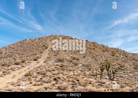Strada sterrata che conduce fino alla cima della montagna del deserto sotto il luminoso cielo blu. Foto Stock