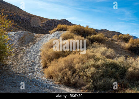 Stretta strada sterrata che conduce sulla collina ripida verso le montagne al di là sotto il luminoso cielo blu. Foto Stock