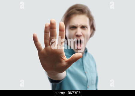 Arrestarlo. Ritratto di angry bello capelli lunghi biondo Uomo in camicia blu in piedi con la mano di arresto gesto segno e guardando la telecamera urlando. interna Foto Stock
