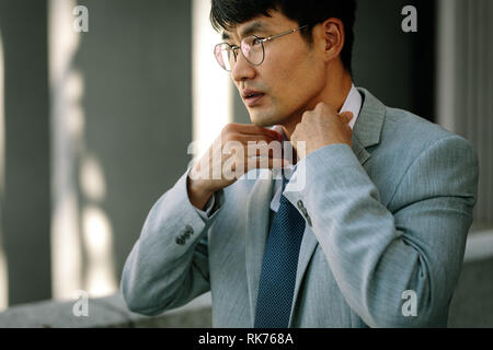 uomo d'affari che si adatta alla cravatta. Asiatico business professionale in tuta regolando la sua cravatta. Foto Stock