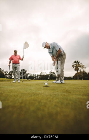 Professional Golfers giocando a golf insieme sul corso senior golfista rendendo un colpo sul verde con altri player in piedi in background holdin Foto Stock