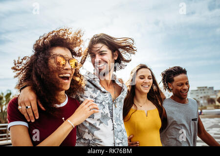 Un gruppo di uomini e donne a piedi giù per la strada a parlare e divertirsi. Multi-etnico amici camminando insieme all'aperto. Foto Stock