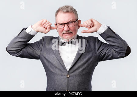Senior uomo chiudendo le orecchie con le dita che non vogliono sentire qualcosa. Foto Stock