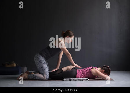 Pullman ad aiutare la donna a praticare yoga, facendo Bhekasana esercitare insieme Foto Stock