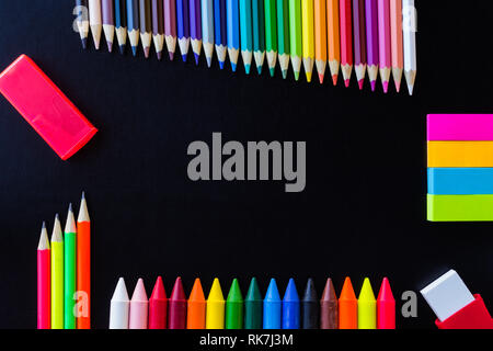 Scuola di disegno e fornisce su sfondo nero. Matite colorate, matite nota adesiva, gomma temperino e pastelli. Con copia spazio. Foto Stock